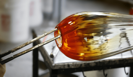Transparent/orange blown glass piece being shaped with metal tools