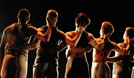 Five modern dancers onstage in silhouette linking arms.